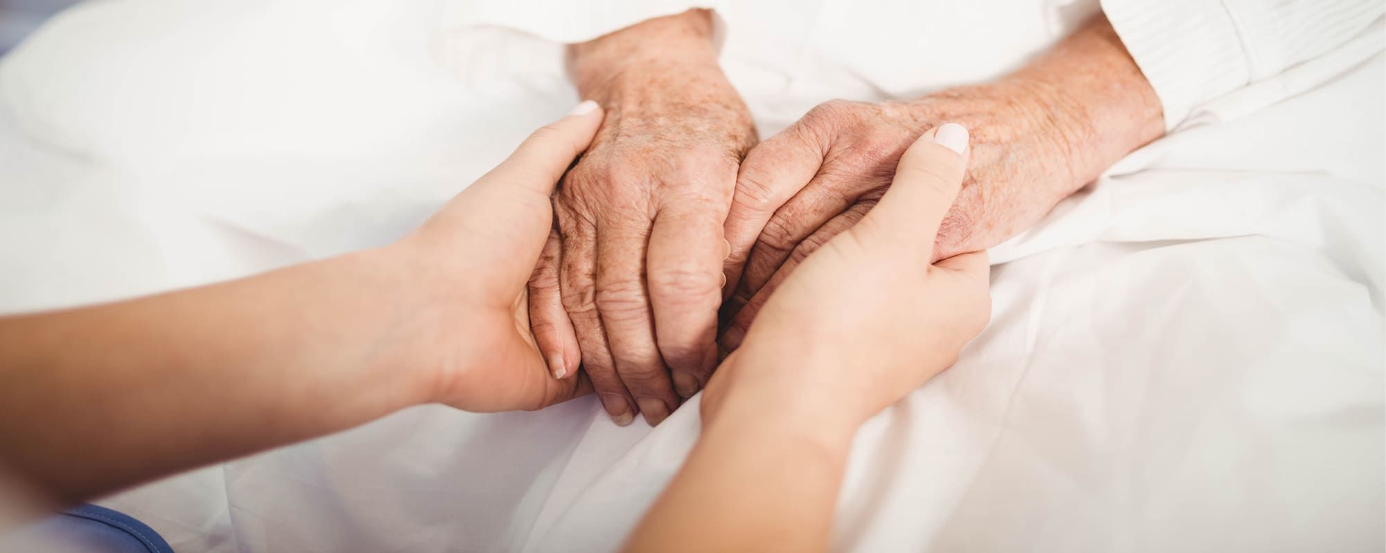 Junge Pflegerin hält einfühlsam die Hände einer älteren Person